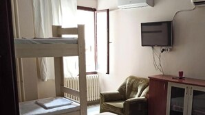 Quarto com cama beliche, cama de solteiro, televisão, armário e radiador.