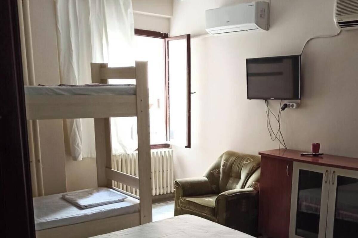 A room with a bunk bed, a single bed, a television, a cabinet, and a radiator.
