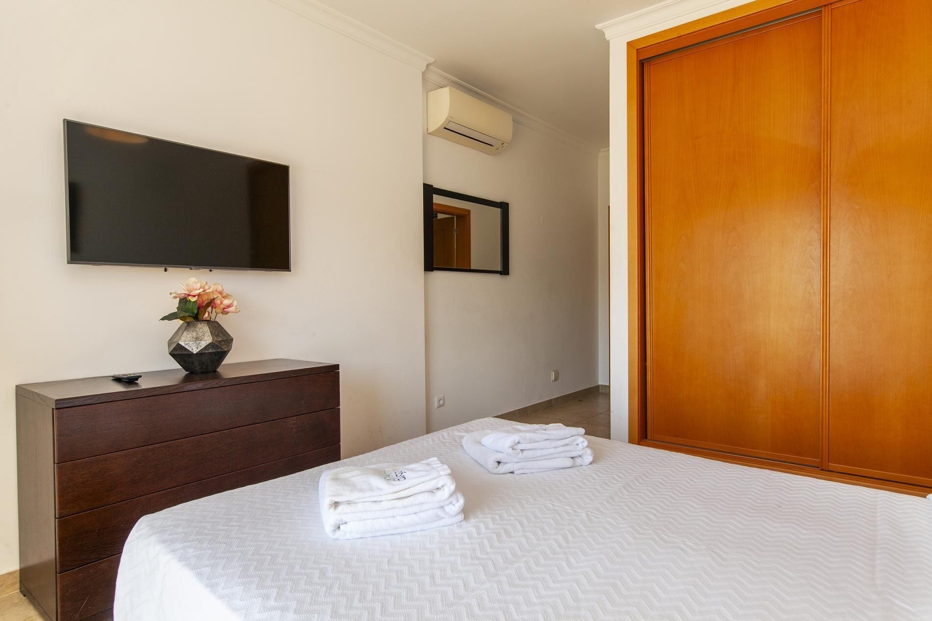 A hotel room with a bed, a dresser, a TV, an air conditioner, a mirror, and a wooden wardrobe.