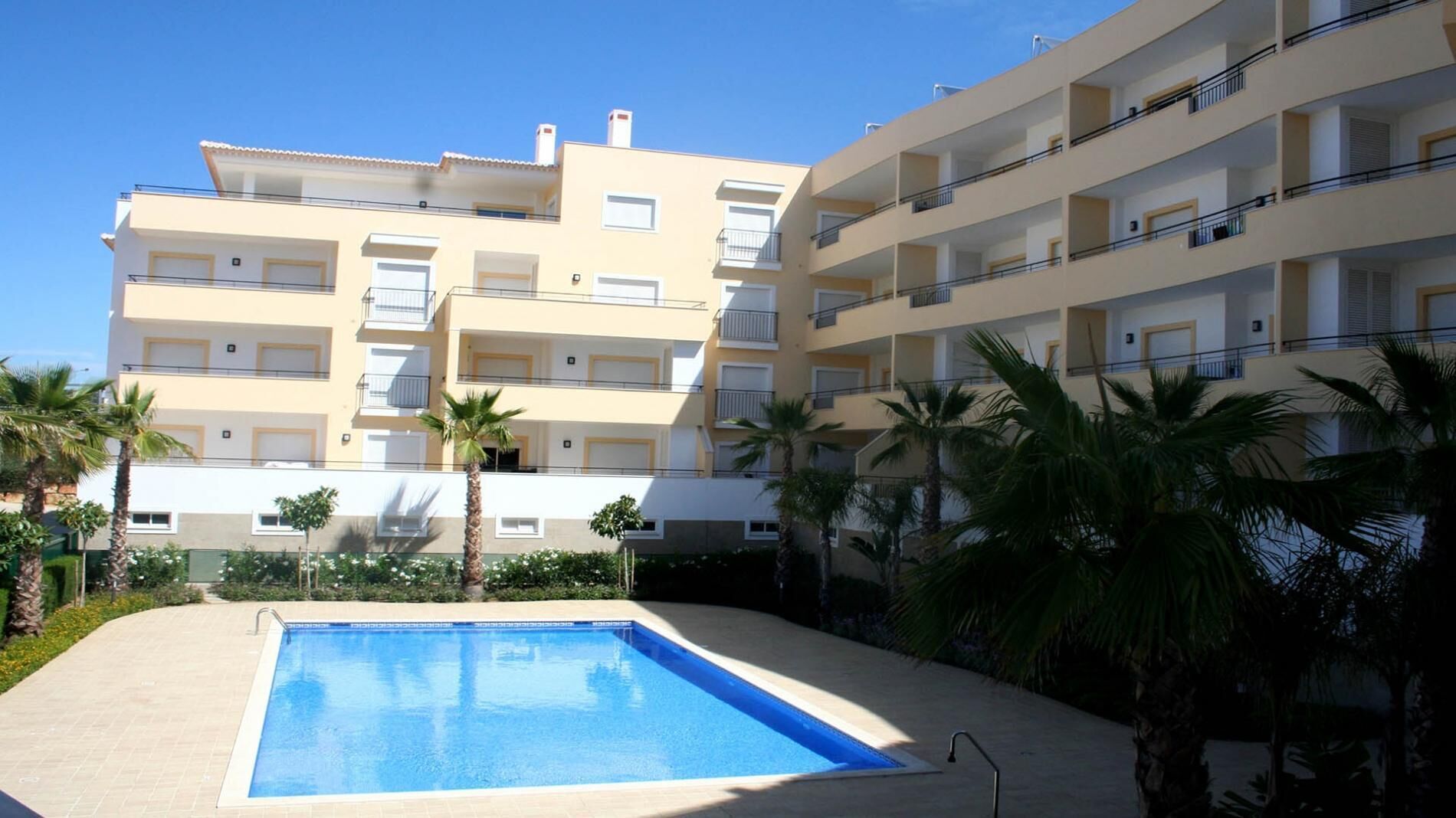 A multi-story residential building with balconies, a swimming pool, and palm trees.