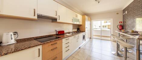 A modern kitchen with white cabinets, a granite countertop, a built-in oven, and a red toaster.