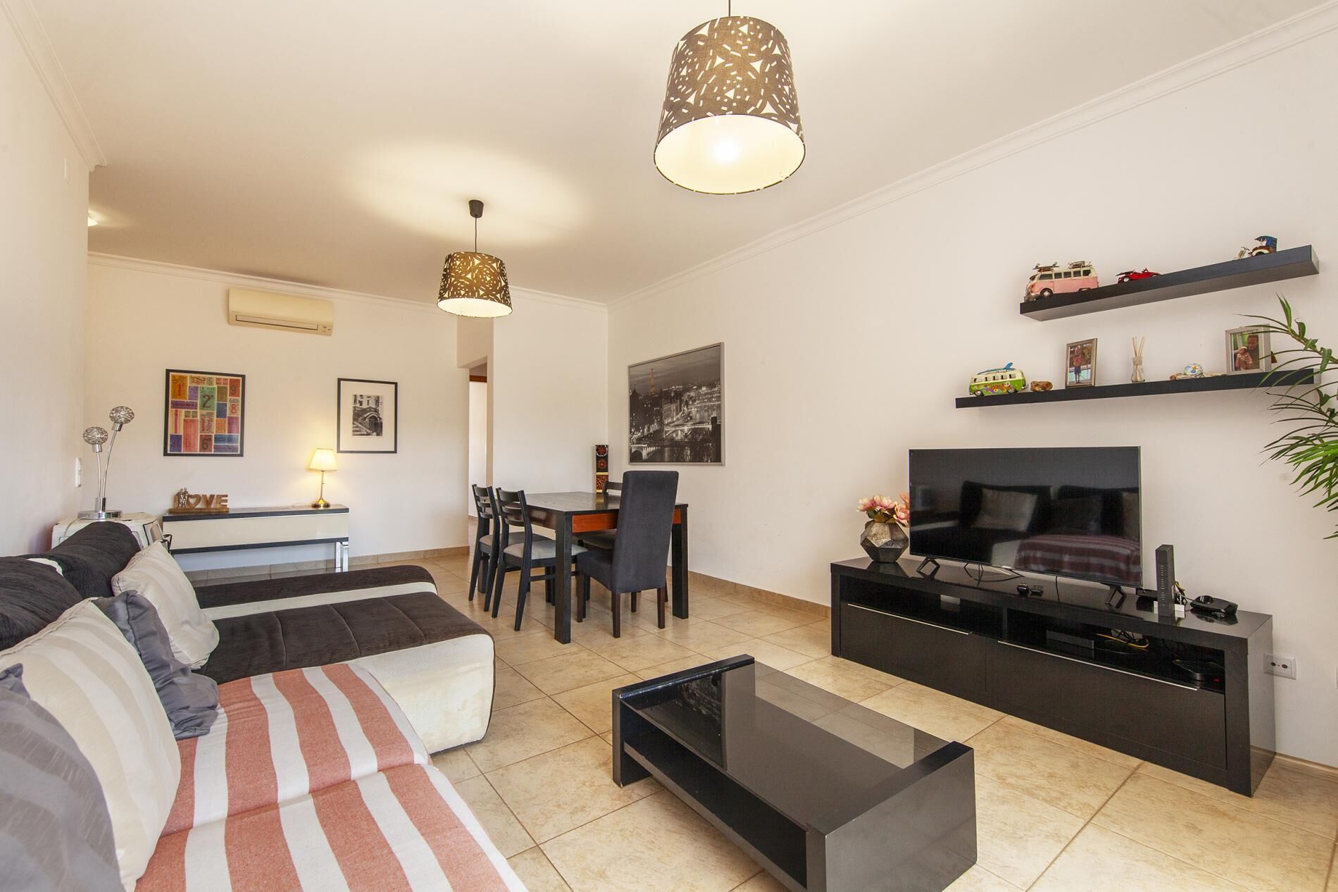 Uma sala de estar moderna com um sofá, uma mesa de jantar, cadeiras, uma televisão e uma mesa de centro.