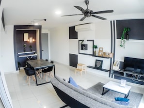 A modern living room with a sofa, a dining table, and chairs. There is a ceiling fan, a TV, and a small plant on a shelf.