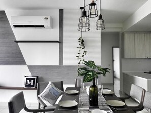 A modern dining area with a table set for four, a potted plant, and hanging pendant lights.