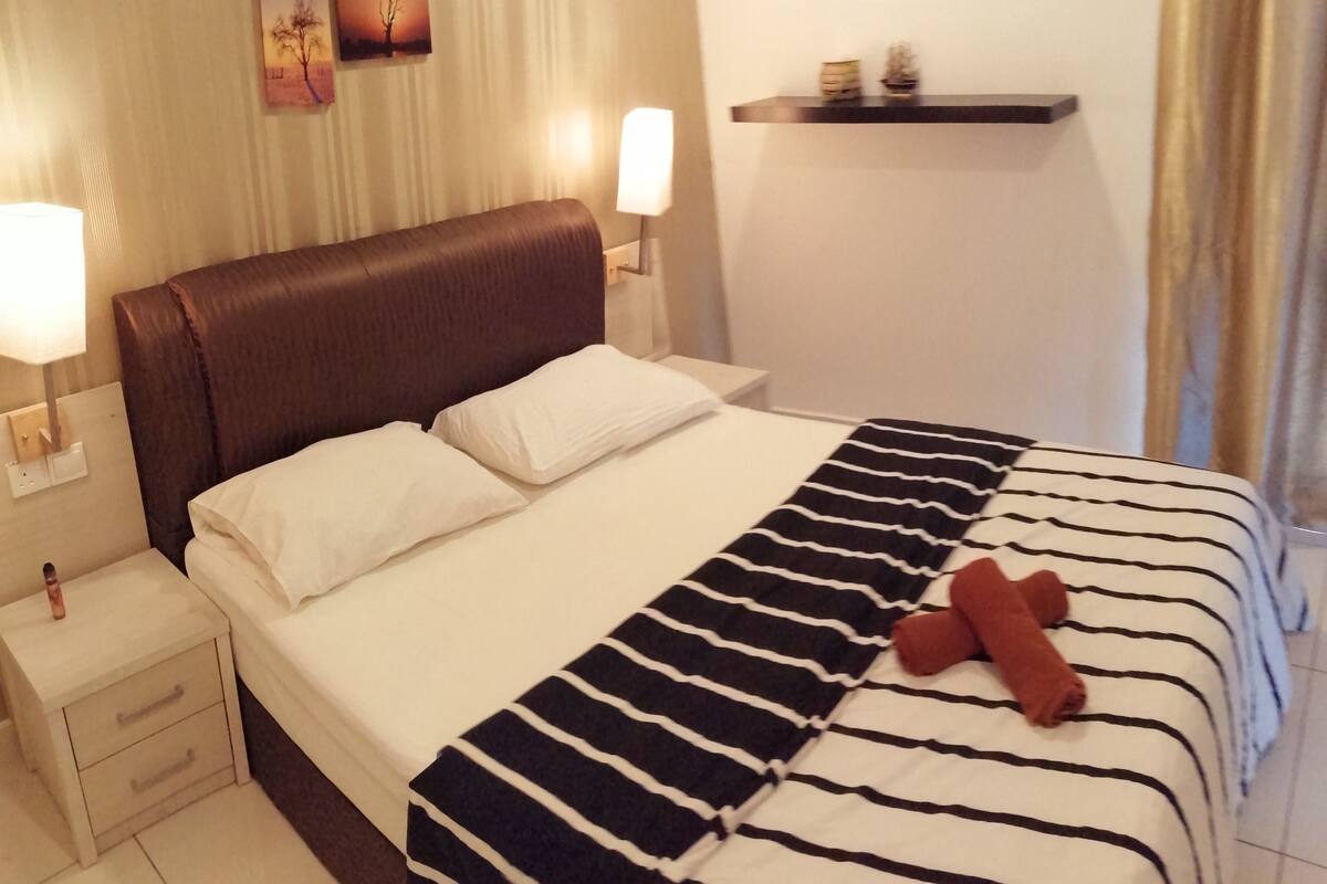 A hotel room with a bed, nightstands, a lamp, a wall-mounted shelf, and a window with curtains.