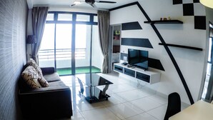 A modern living room with a sofa, a TV on a white stand, and a dining area with a table and chairs.