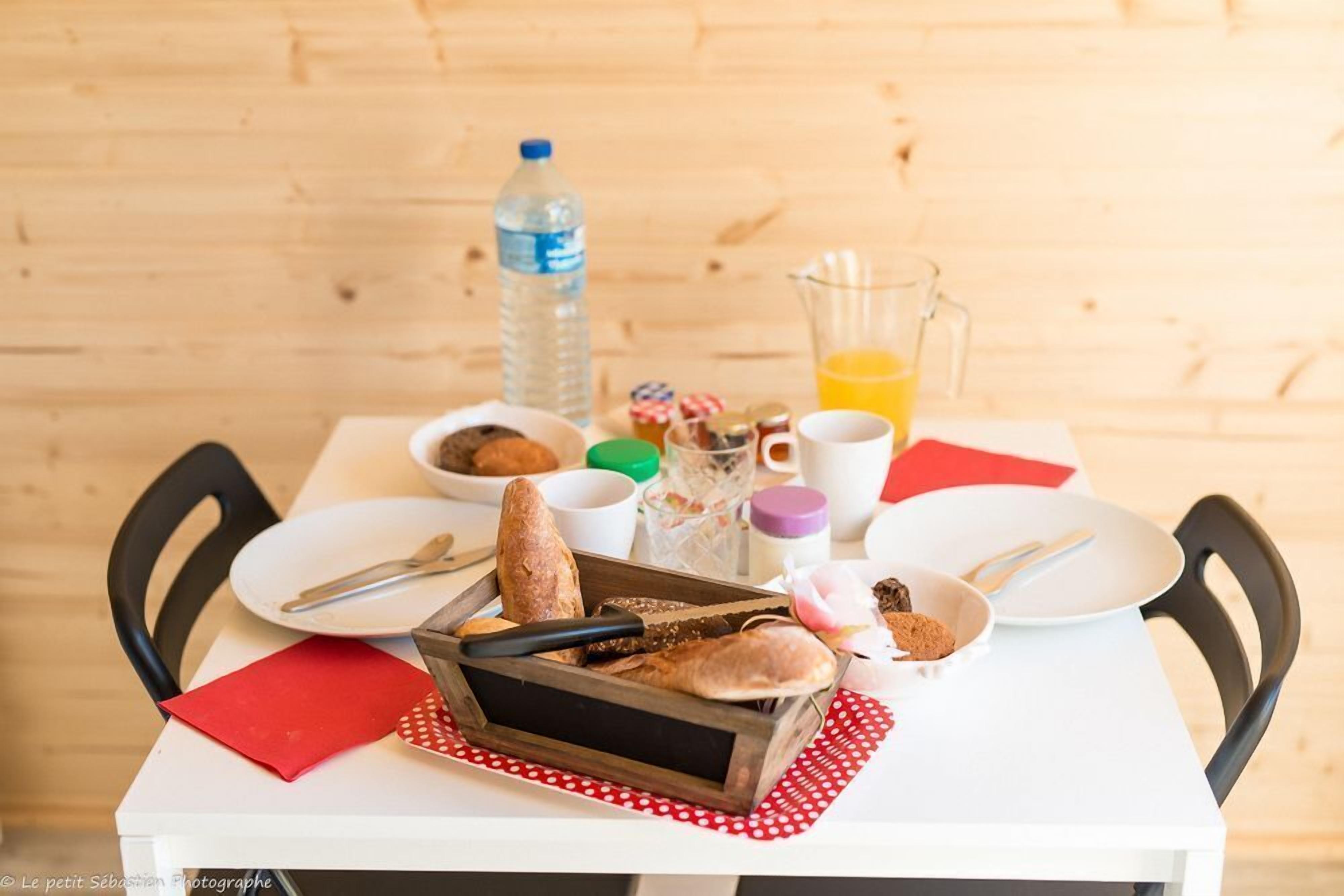 Une table de petit-déjeuner avec du pain, une bouteille d’eau, un verre de jus d’orange et une tasse de café.