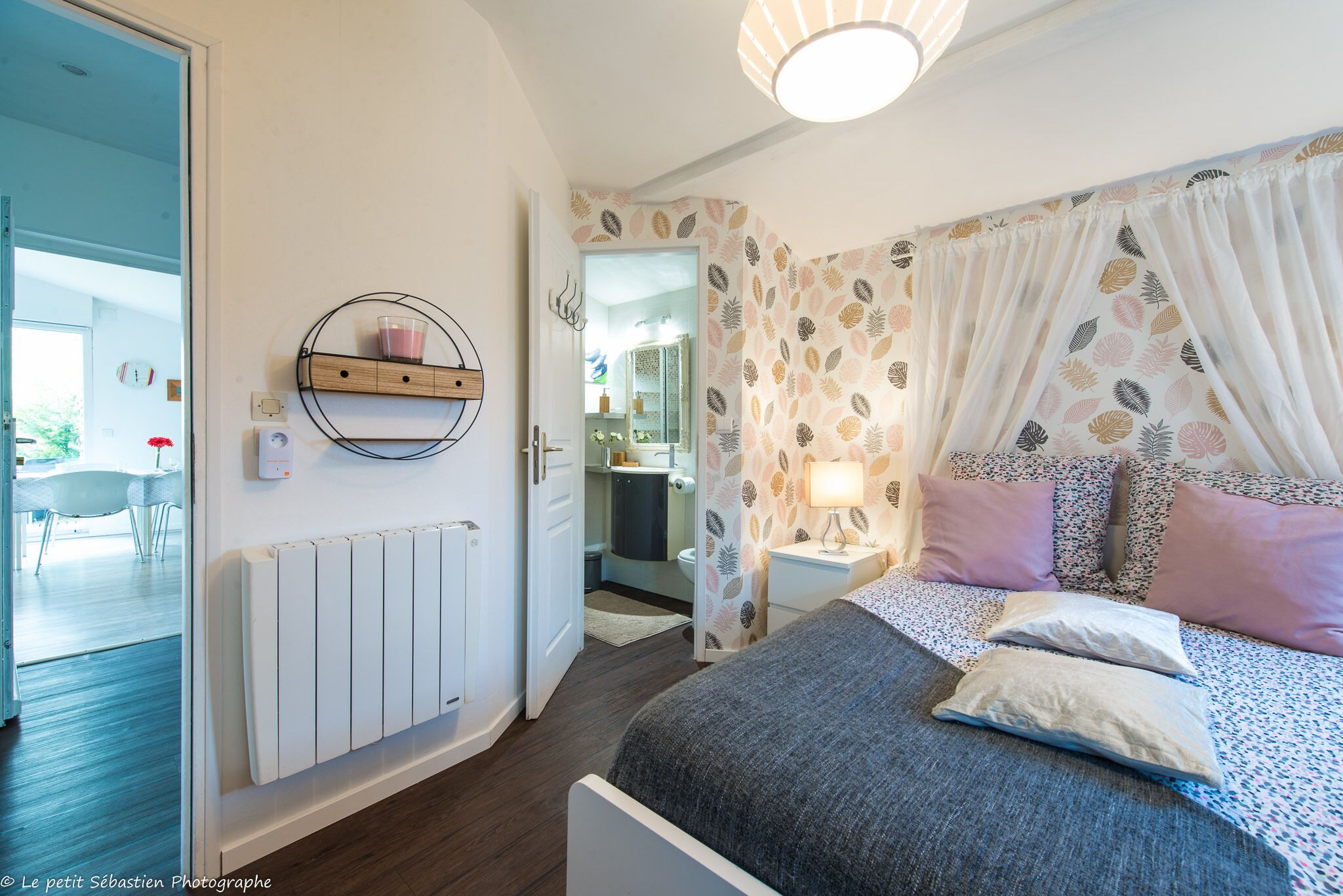 A bedroom with a bed, bedside table, lamp, and a view into the bathroom.
