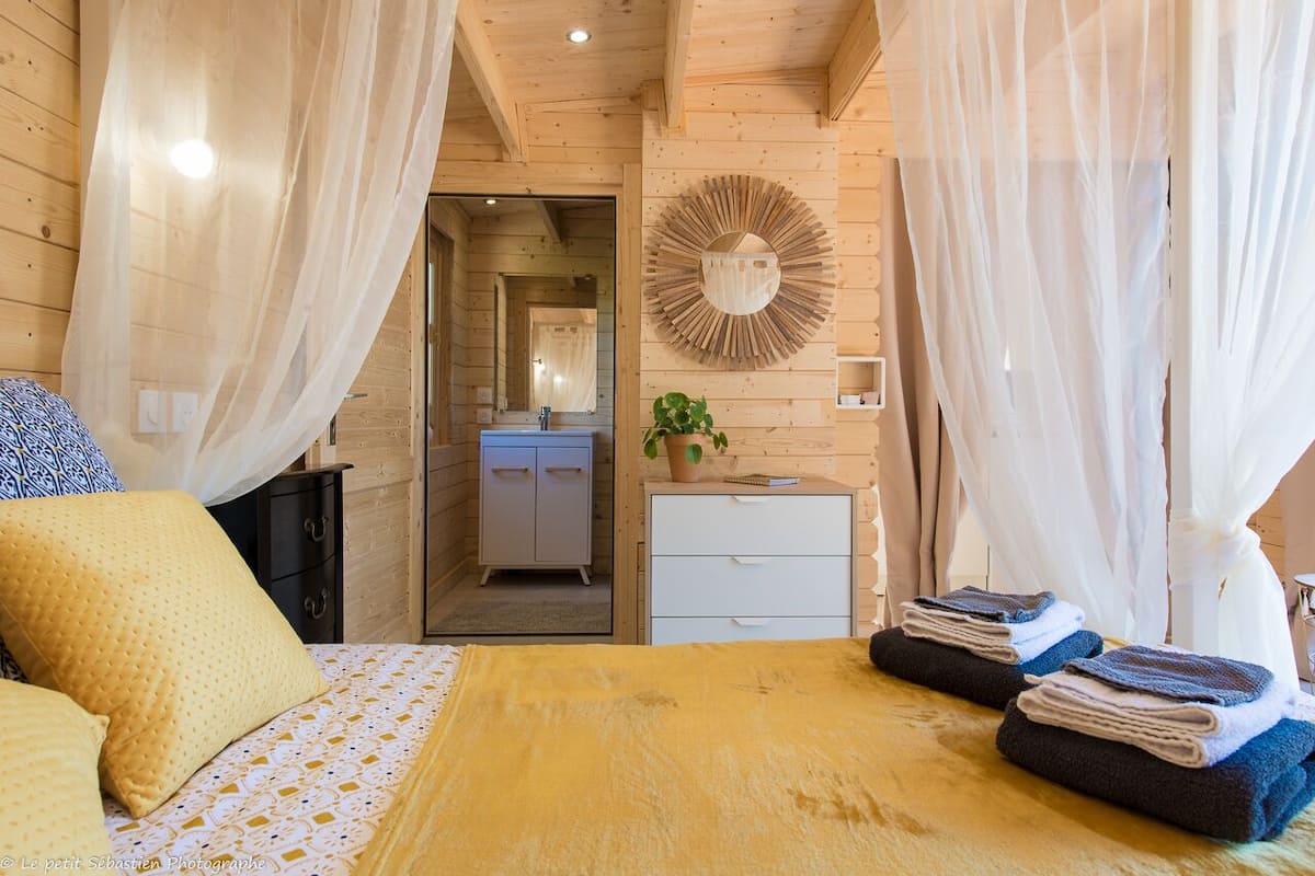A bedroom with a bed, a bedside table, a mirror, and a door leading to a bathroom.
