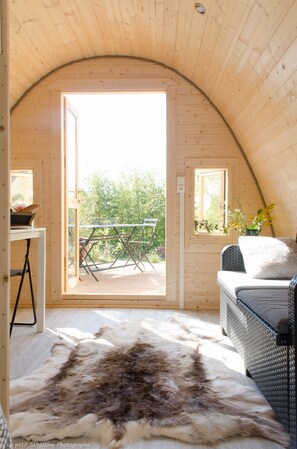 A cozy wooden interior with a large open door leading to an outdoor balcony, a wicker sofa, and a fur rug. - Chambre d'hôtes Le Petit Flo (Flocourt)