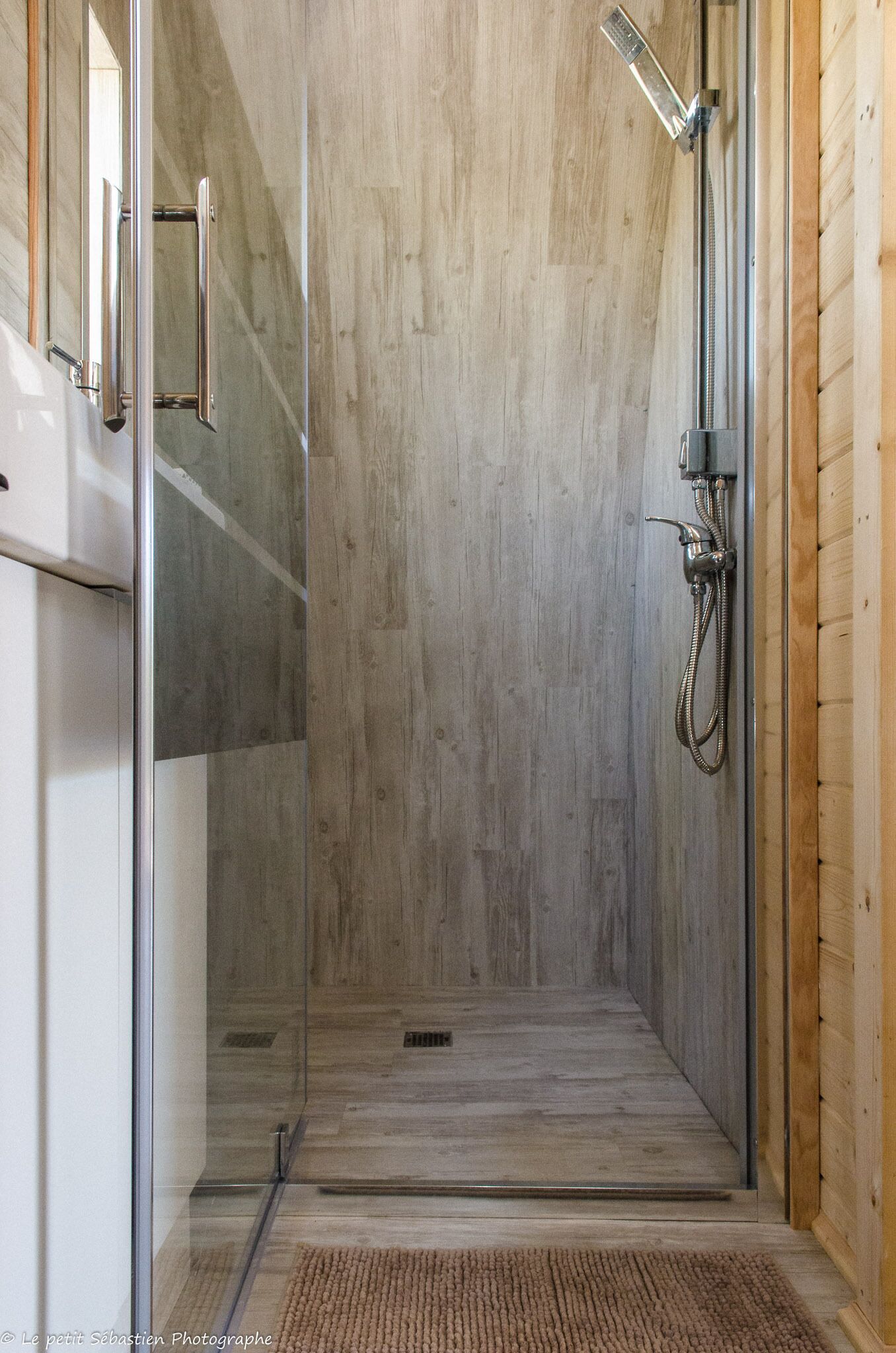 Een douche met glazen wanden, een houten vloer en een metalen douchekop.