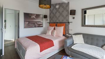 A modern bedroom with a bed, a grey sofa, a large mirror, and a painting on the wall.