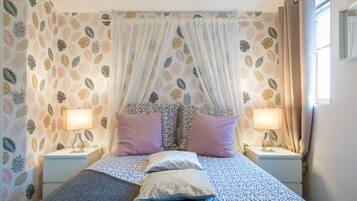 Une chambre à coucher avec un lit à baldaquin, un papier peint à motifs floraux, deux lampes de chevet et une fenêtre avec des rideaux.