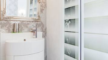 Un baño con tocador blanco, un espejo grande y un box de ducha con vidrio esmerilado.