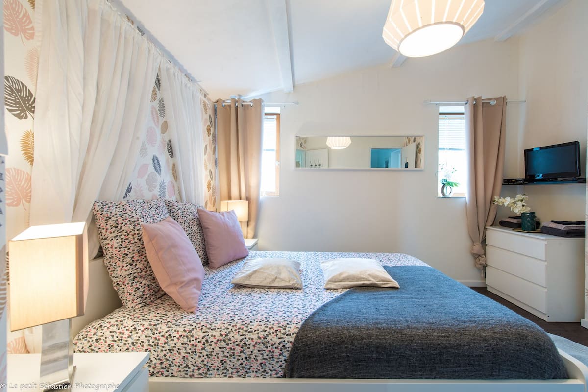 A bedroom with a bed, a bedside table, a lamp, a dresser, a television, and a mirror.