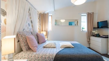 Ein Schlafzimmer mit Bett, Nachttisch, Lampe, Kommode, Fernseher und Spiegel.