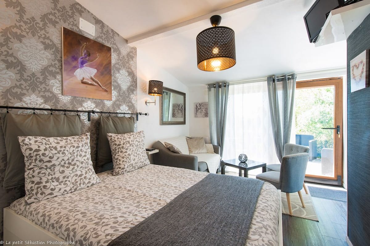 A bedroom with a large bed, a sitting area with a table and chairs, a painting on the wall, and a window with curtains.