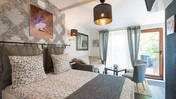 A bedroom with a large bed, a sitting area with a table and chairs, a painting on the wall, and a window with curtains.