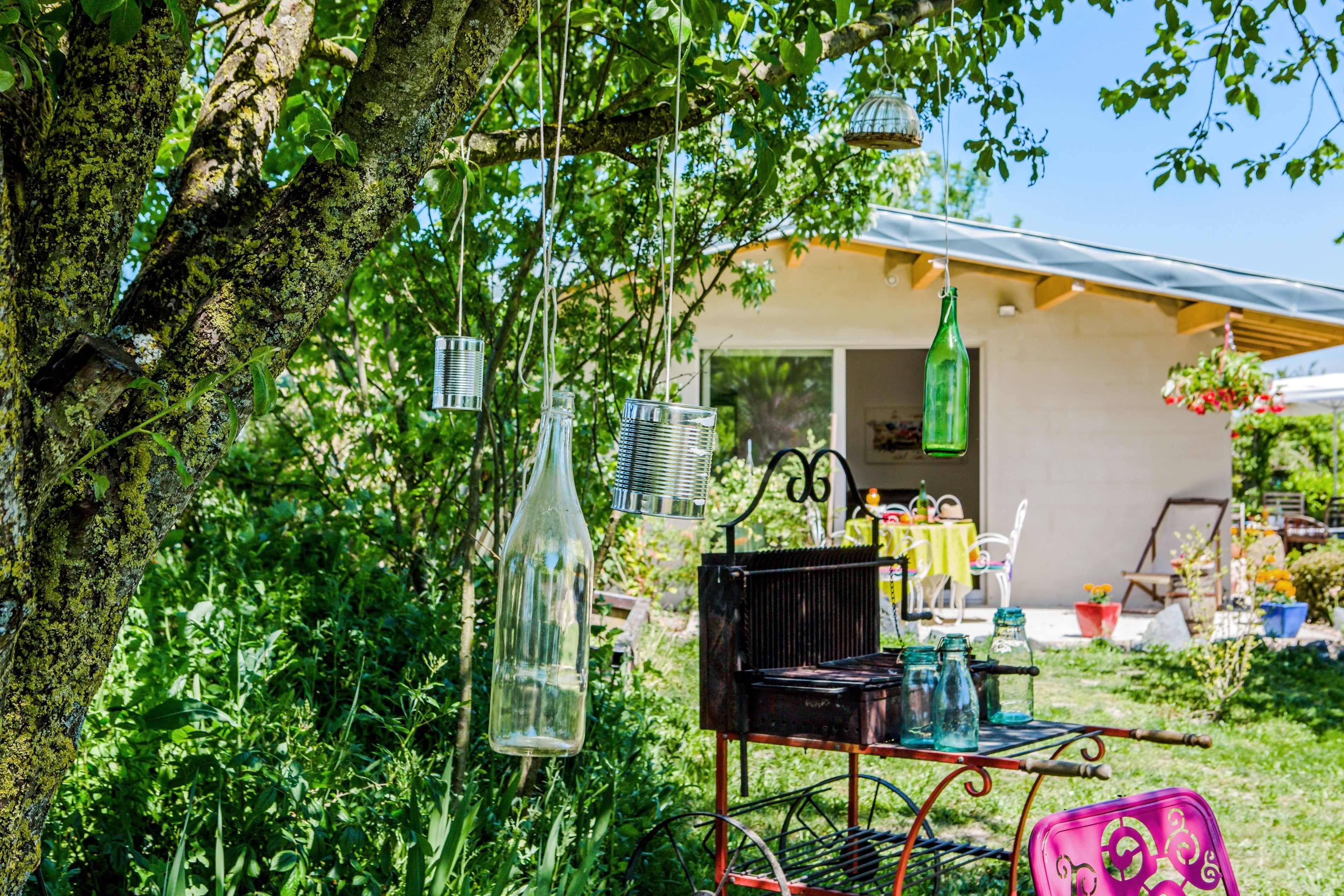 A rustic outdoor setting with a metal cart, hanging glass bottles, and a tree.