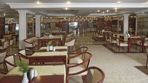 A spacious dining area with multiple tables and chairs, a central kitchen area, and a view of the dining space through glass partitions. - Grand Hotel Temizel (Ayvalik)