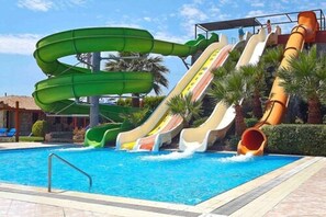 Una piscina con múltiples toboganes acuáticos, incluyendo un tobogán en espiral verde y varios toboganes rectos de diferentes colores.