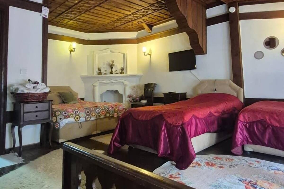 Een rustieke slaapkamer met een houten plafond, een open haard, een televisie en twee bedden met rode beddengoed.