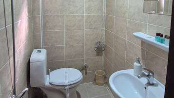 A bathroom with a toilet, sink, shower, and a small window.