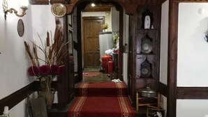 A hallway with a red carpet leading to a room. There is a wooden ceiling with a geometric pattern, a wall-mounted light fixture, and a door at the end of the hallway.