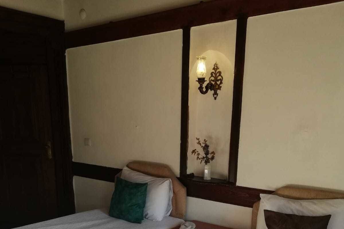 Een kamer met twee bedden, een nachtkastje, een wandlamp en een deur.