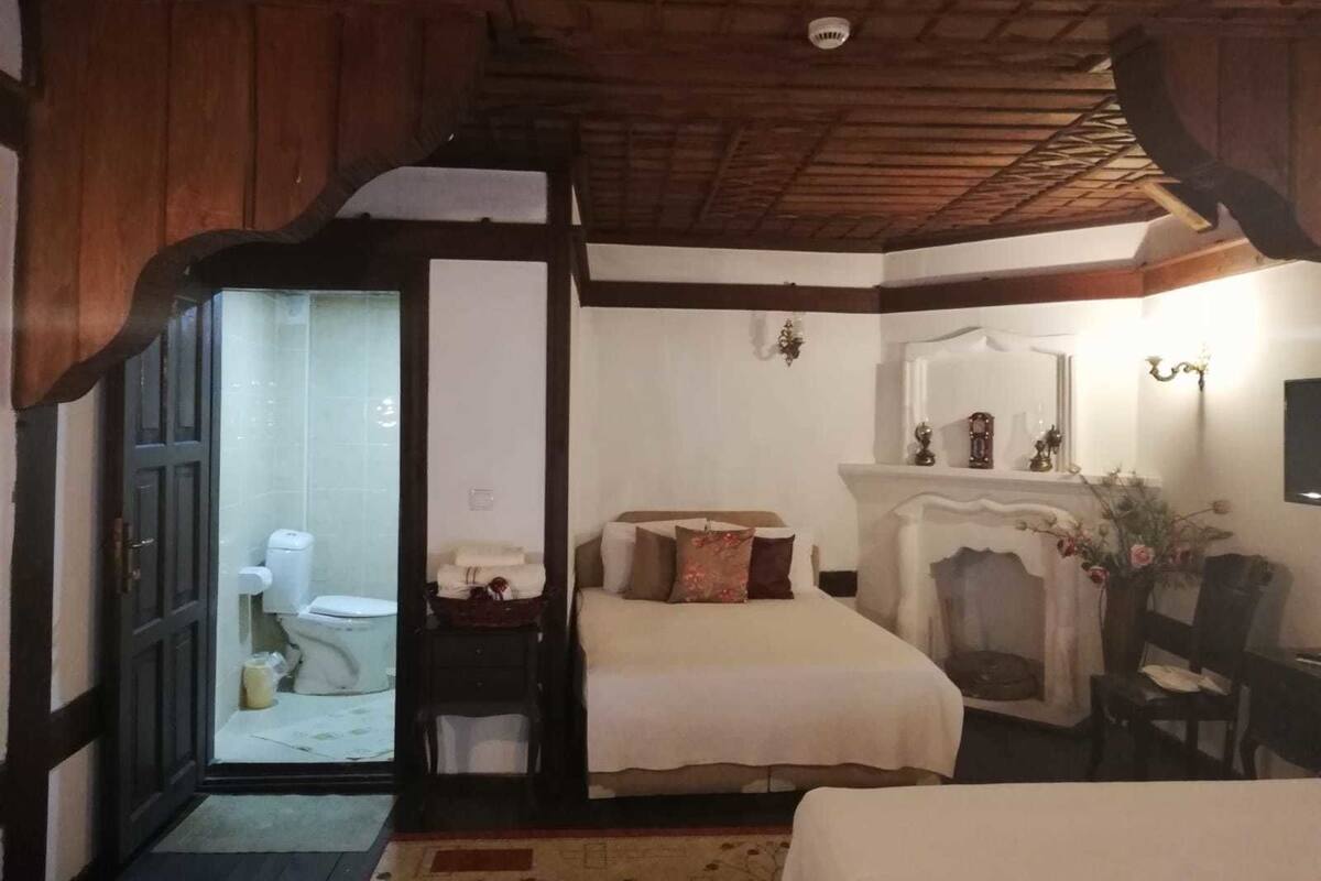 Een slaapkamer met een houten plafond, een bed, een nachtkastje, een stoel, een open haard en een deur naar een badkamer.