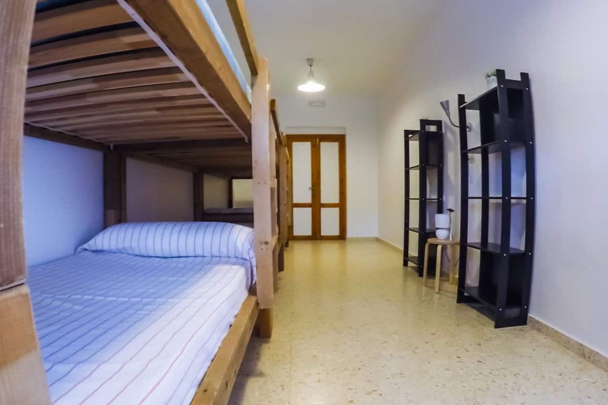A room with a bunk bed, a wooden door, a black shelving unit, and a tiled floor.