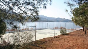A fenced tennis court with a view of a lake and mountains in the background. - Alojamiento Rural Lago de Andalucía - Hostel (Iznajar)