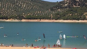 A beach with people engaging in water activities, boats, and a hilly landscape in the background. - Alojamiento Rural Lago de Andalucía - Hostel (Iznajar)