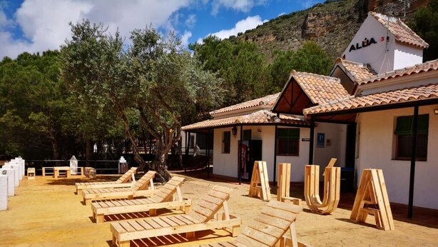 A sunlit outdoor area with wooden lounge chairs and a building with a tiled roof. - Alojamiento Rural Lago de Andalucía - Hostel (Iznajar)