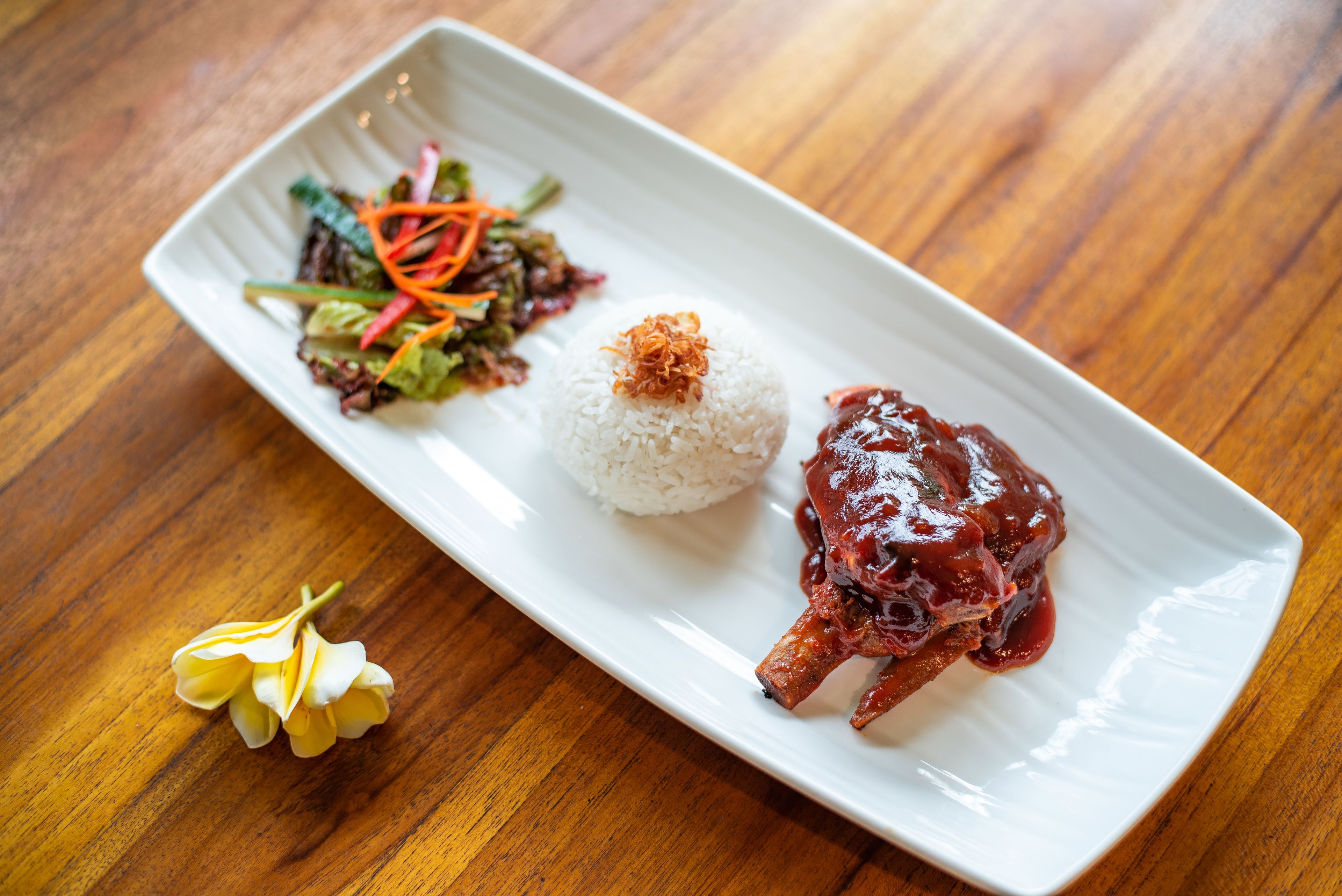 Un plato rectangular blanco con arroz blanco, salsa roja y una ensalada de verduras sobre una mesa de madera.