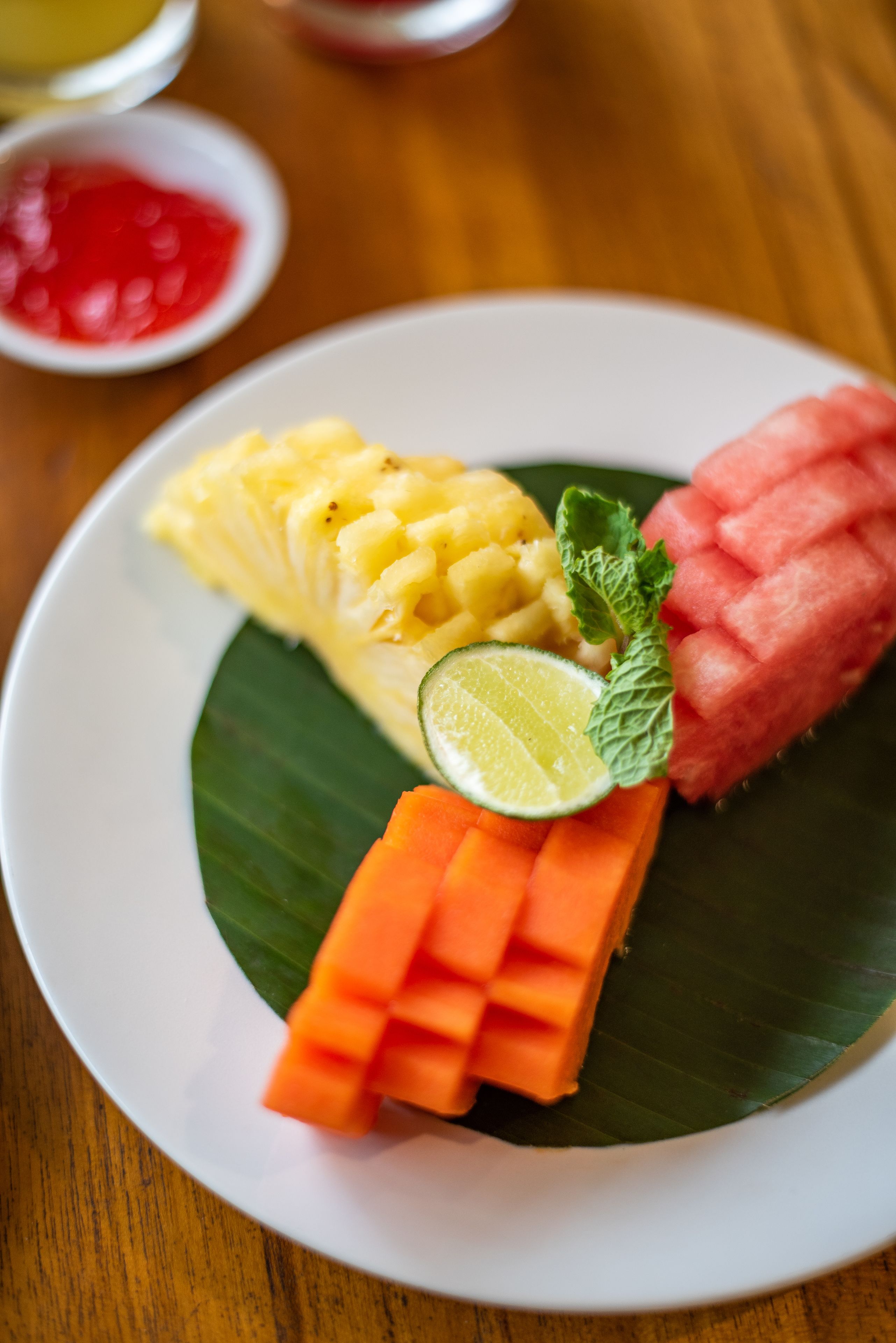A plate with pineapple, mango, and carrot slices on a banana leaf.