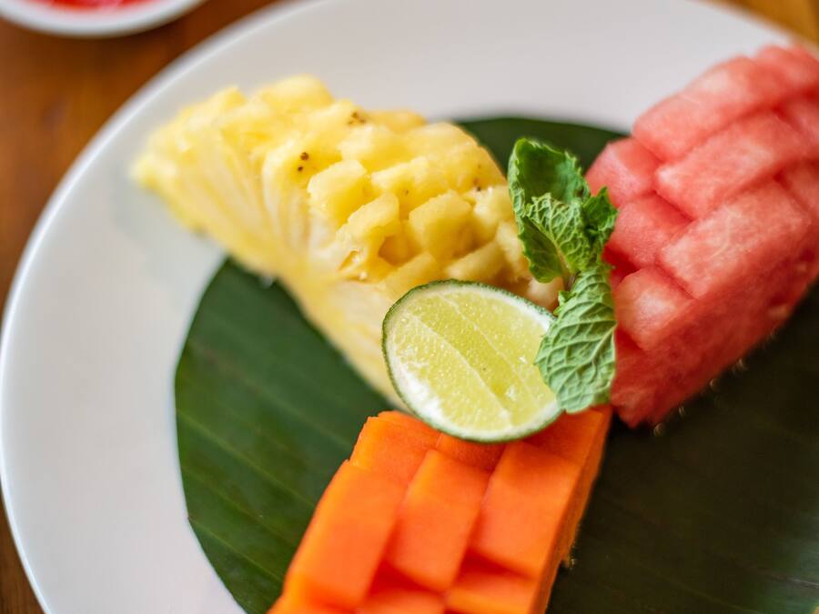 Un plato con trozos de piña, mango y zanahoria sobre una hoja de plátano.