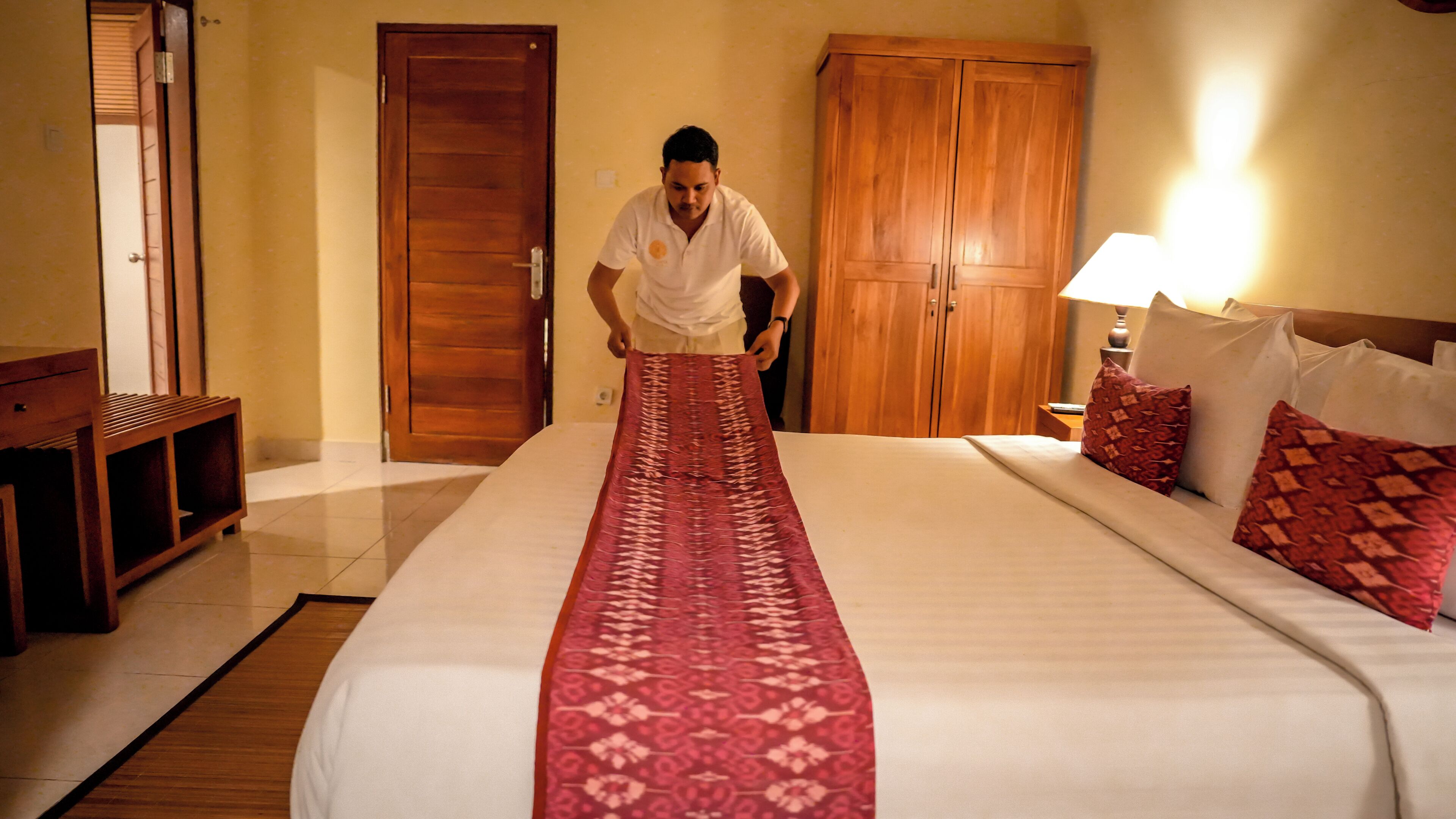 A hotel room with a bed, a wooden wardrobe, a nightstand, and a lamp.