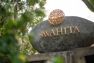 A stone with the name 'SWAHITA' engraved on it, surrounded by greenery.