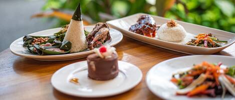 A variety of dishes on plates, including rice, meat, and vegetables, arranged on a wooden table.