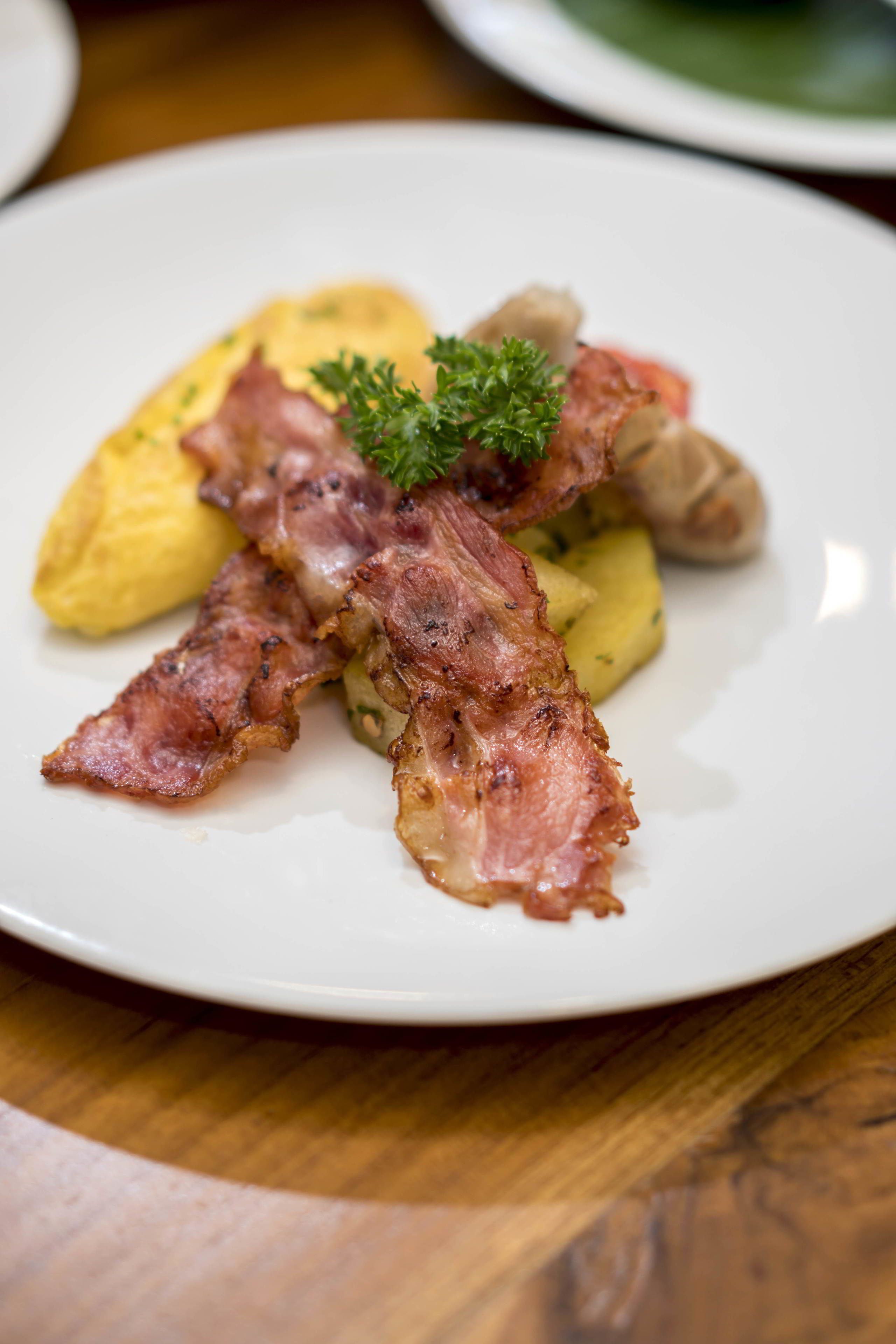 A plate with bacon, potatoes, and a garnish on a white plate.