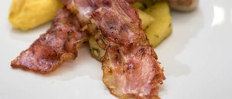Un plato con tocino, papas y una guarnición sobre un plato blanco.