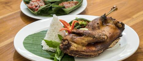 A plate with a roasted duck, rice, and vegetables on a wooden table.