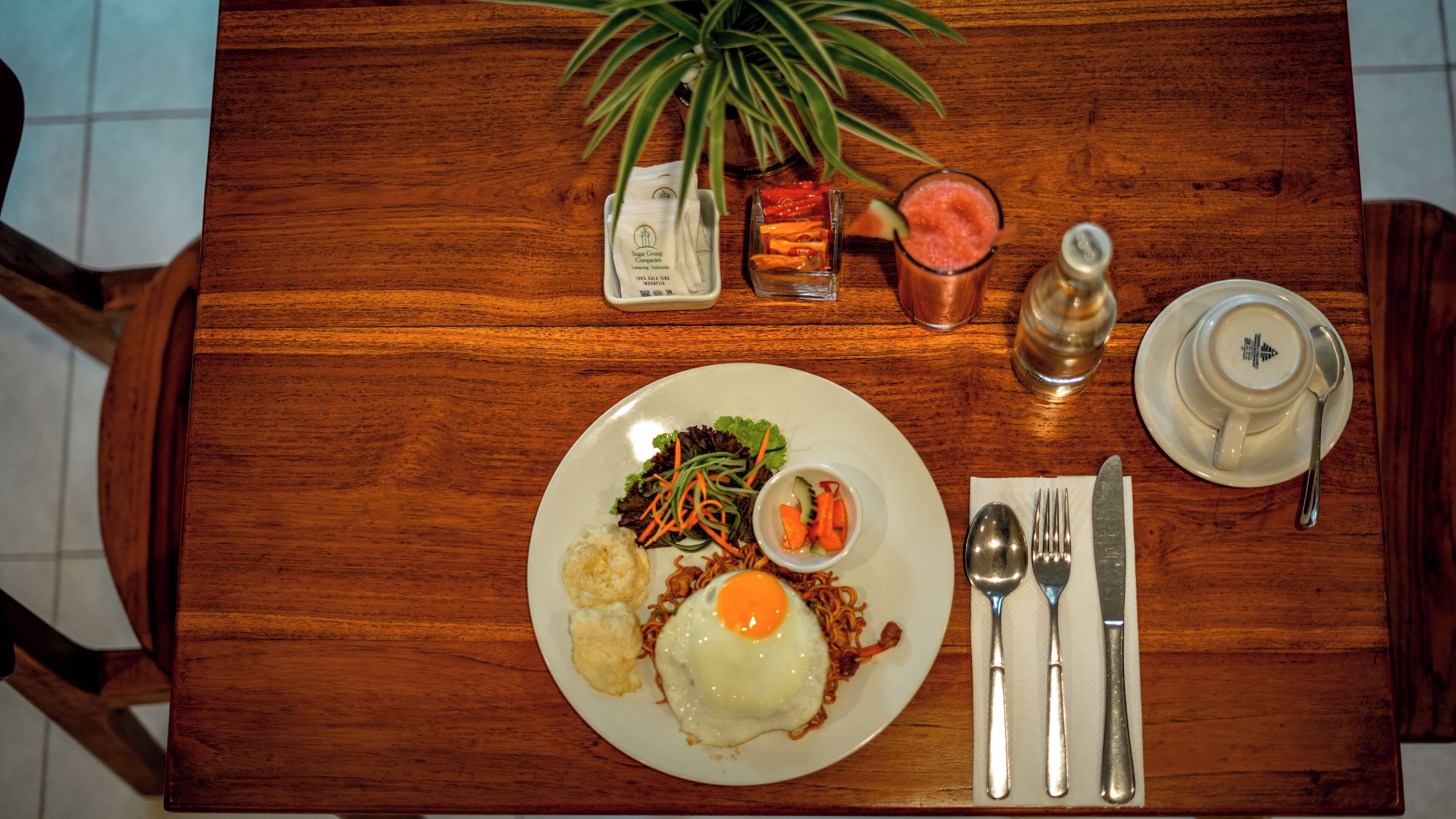 A wooden table with a plate of food, a glass of drink, and a bottle of water.