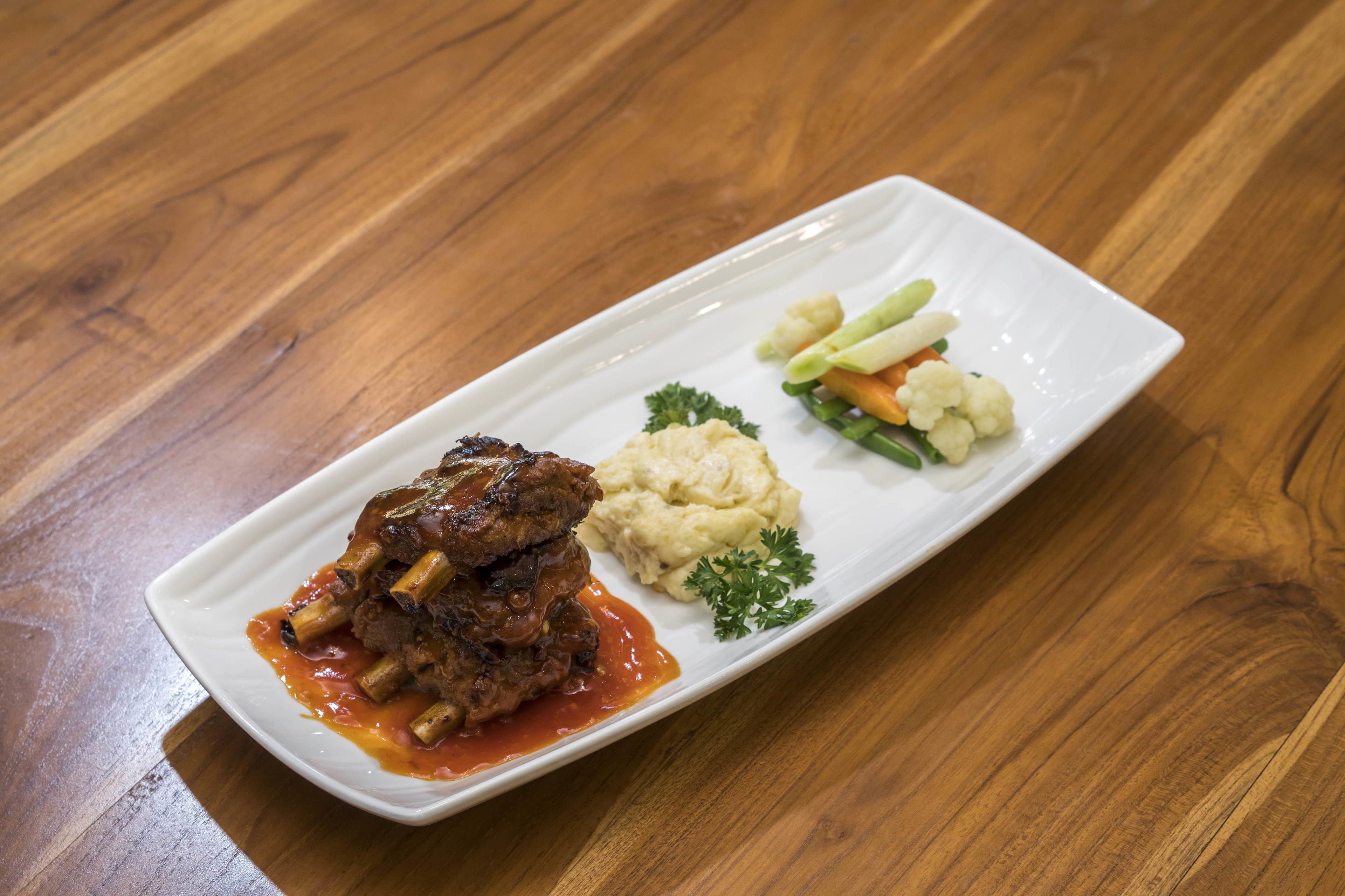 A rectangular white plate with a meat dish, mashed potatoes, and steamed vegetables on a wooden table.