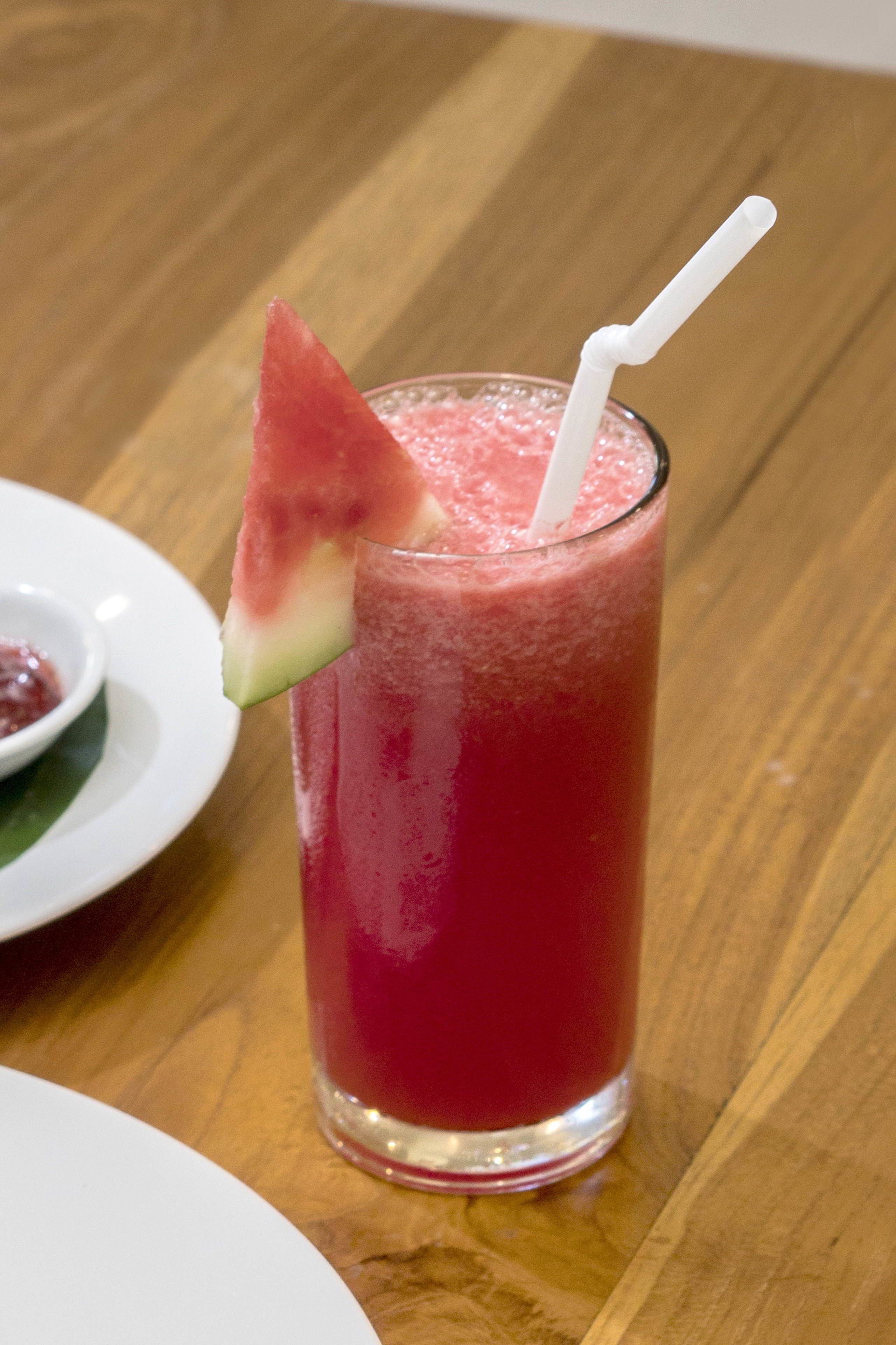 A glass of red beverage with a watermelon slice and straw on a wooden table.