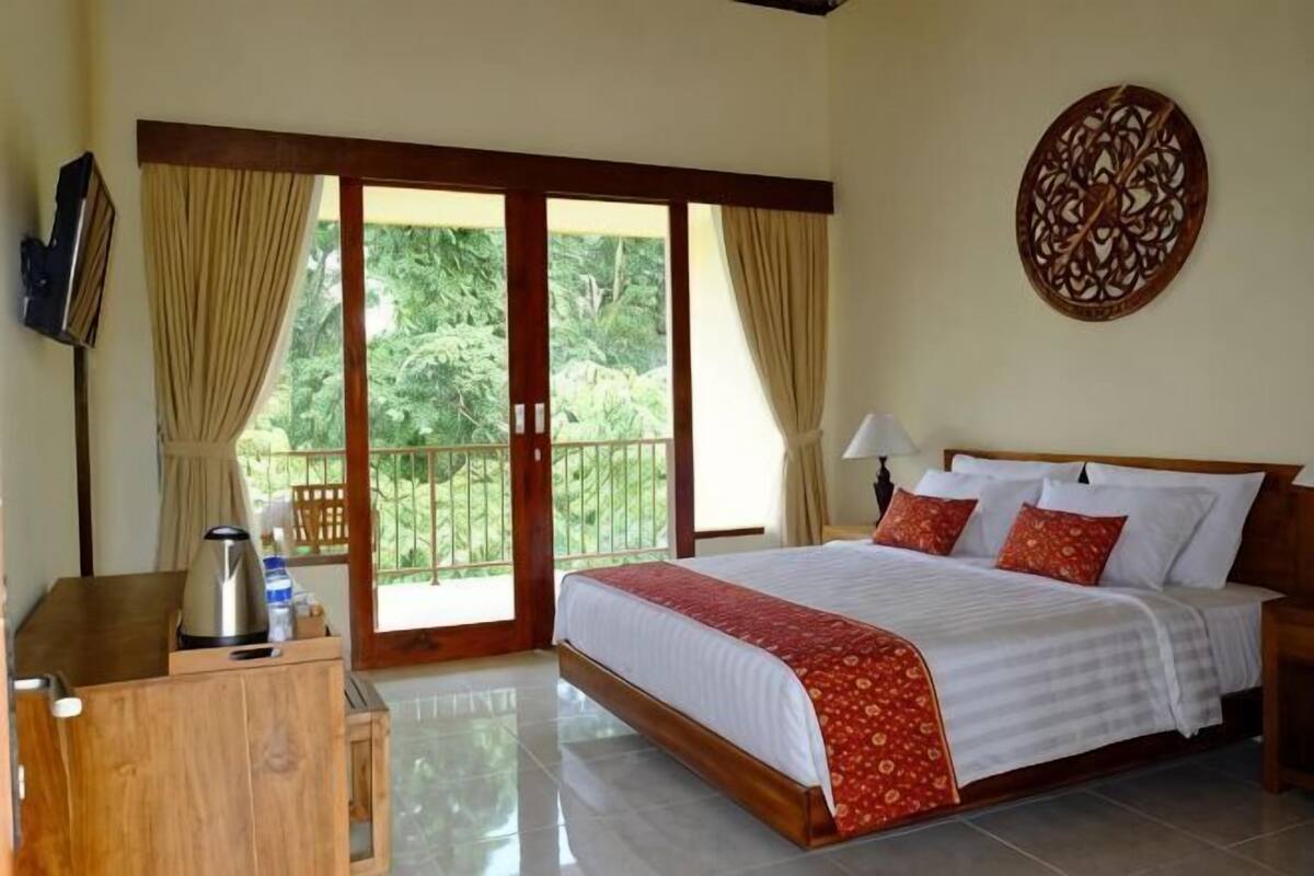 A bedroom with a bed, a wooden dresser, a TV, and a balcony with curtains.