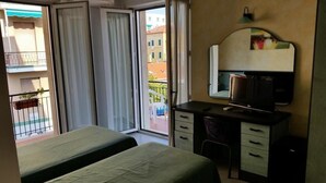 A hotel room with a bed, a desk with a chair, a mirror, and a window with curtains. - Hotel San Nazario (Varazze)