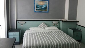 A bedroom with a bed, bedside tables, a nightstand, a painting on the wall, and a window. - Hotel San Nazario (Varazze)
