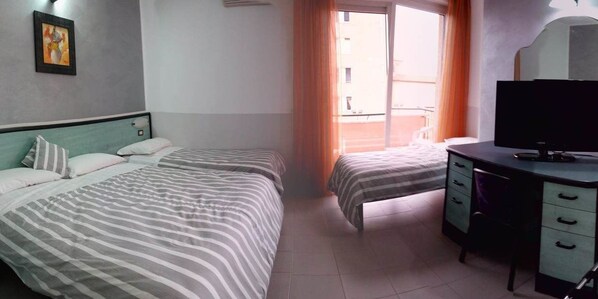 Ein Hotelzimmer mit zwei Betten, einem Schreibtisch, einem Fernseher und einem Fenster mit Vorhängen.